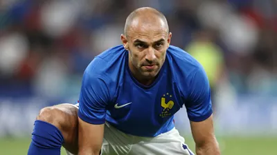 A photorealistic image of a 40-year-old man with a shaved head, wearing a France team goalkeeper's kit (blue shirt, white...