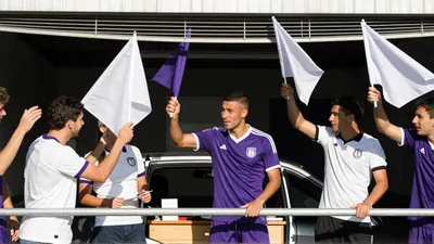 Ibrahim Cissoko, mid-30s, muscular forward, sprinting on a rain-slicked pitch, wearing a plain violet jersey and white...
