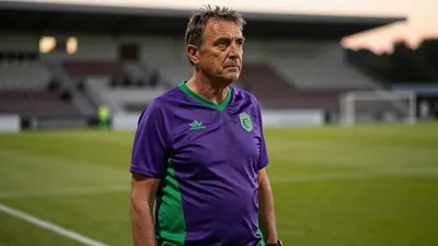 A 50-year-old male coach with a rugged build, standing on the edge of the Stadium de Toulouse pitch, his weathered face...
