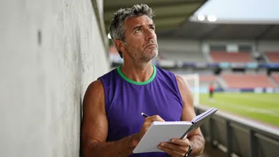 A 35-year-old, ruggedly-built, athletic coach with a strong jawline and a few wisps of graying hair, intensely focused...