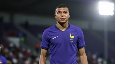 A 20-year-old French footballer with short dark hair and a lean build, wearing a solid purple jersey, photographed with...