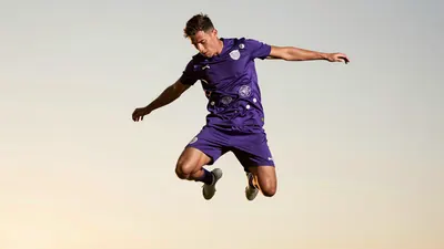 A male Toulouse FC player in his early 20s, muscular build, wearing the new away kit in solid violet with reflective 3D...
