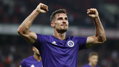 A muscular 25-year-old Toulouse Football Club forward in a solid purple jersey, mid-celebration after scoring, arms...