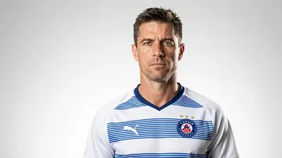 A 43-year-old Danish coach with a strong jawline and a determined look, wearing a white Toulouse Football Club jersey...
